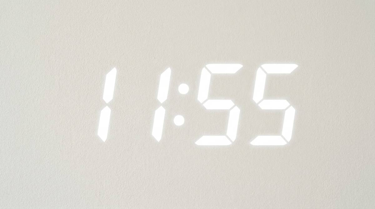 Wyświetlacz cyfrowego zegara pokazujący godzinę 11:55 na jasnym, jednolitym tle.