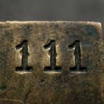 Sekwencja cyfr 111 wybita ręcznie w patynowanym mosiądzu, oświetlona ciepłym bocznym światłem