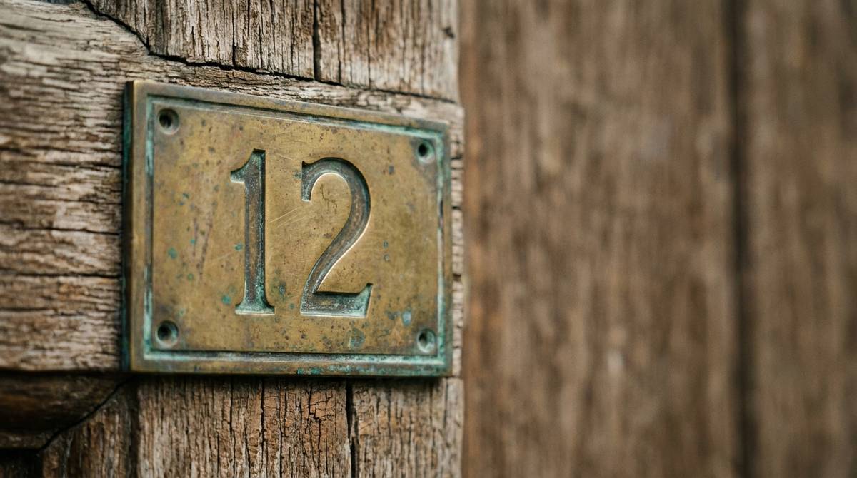 Mosiężna tabliczka z wygrawerowaną liczbą 12 na tle starych drewnianych drzwi