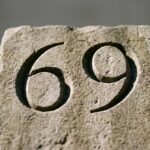 Cyfry 69 wykute dłutem w kamiennej płycie, oświetlone bocznym naturalnym światłem