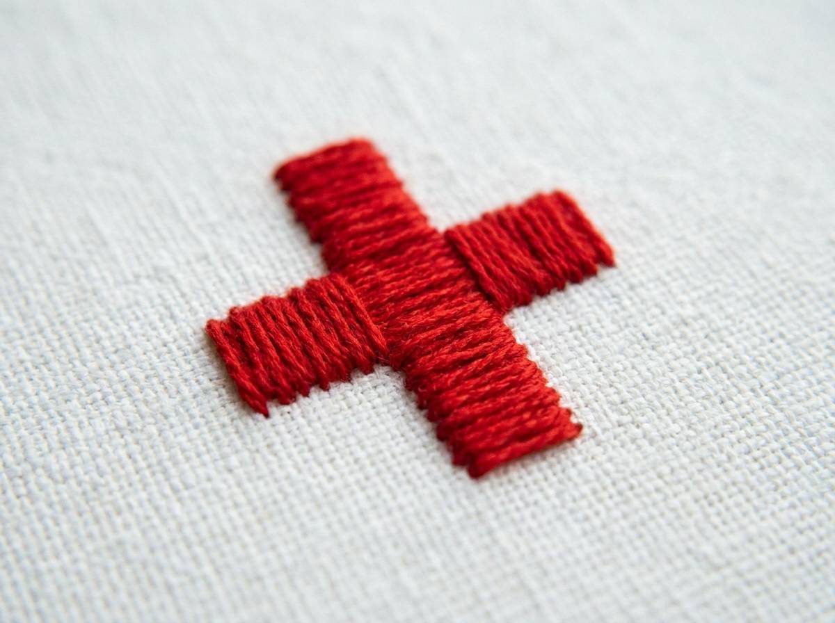 Czerwony krzyż naszyty na białym płótnie, neutralny znak ochrony personelu medycznego.