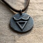 Metalowy wisiorek ze znakiem Welesa w kształcie trójkąta z wygiętymi rogami na skórzanym rzemyku