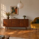 Salon retro z orzechową komodą na smukłych nóżkach, musztardowym fotelem, mleczną kulą i parkietem w jodełkę